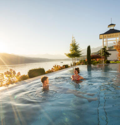 Badehaus_MillstätterSee_MBN_©FranzGerdl_Herbst2022_14 Zwei Personen in einem Außenpool am Ufer eines Sees bei Sonnenuntergang.