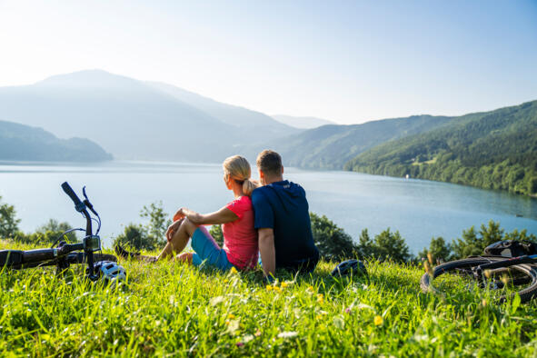Seenschleife_MillstätterSee_MBN_©GertPerauer Zwei Radfahrende blicken auf einen Kärntner See vor Bergkulisse