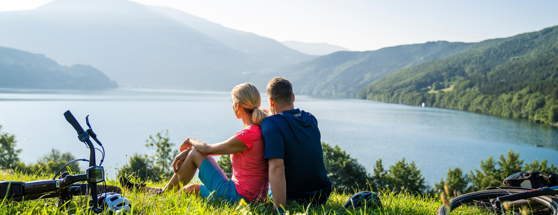 Seenschleife_MillstätterSee_MBN_©GertPerauer Zwei Radfahrende blicken auf einen Kärntner See vor Bergkulisse