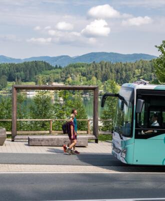 Mobil-Bus-Klopeiner-See-©Stabentheiner_web Zwei Personen vor einem Regionalbus an einer Haltestelle vor Seen- und Berglandschaft