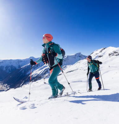 Zwei Personen mit Skiern steigen auf einem verschneiten Berghang auf.