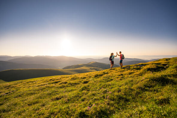 Zwei Wandernde auf einer Almwiese mit Bergpanorama