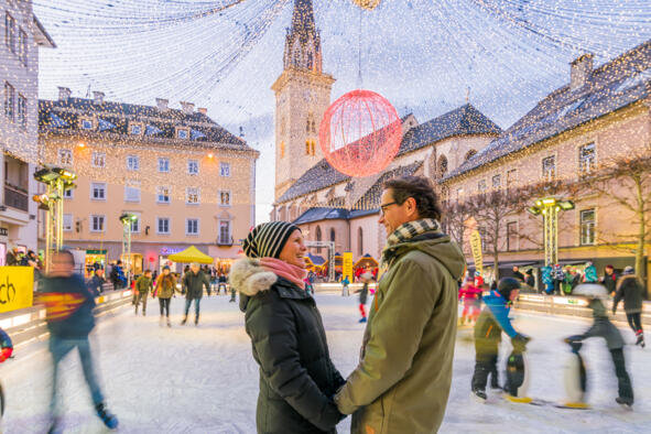 Zwei Personen auf einem festlich beleuchteten Platz mit Eislaufbahn in einer Kärntner Altstadt