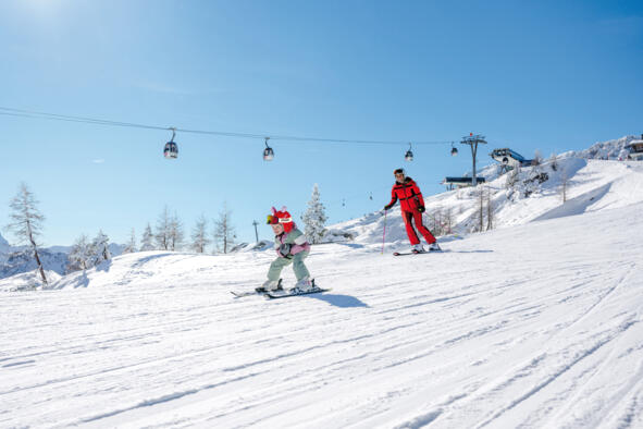 27_Kärnten Werbung GmbH_Michael Stabentheiner Kind und erwachsene Person auf einer Skipiste unter einer Seilbahn